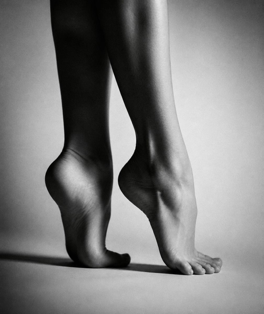 Black and white fine-art study of arched bare feet against a plain backdrop